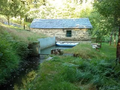 a stone house with a boat in a river at Molino de Louzao in Palas de Rei