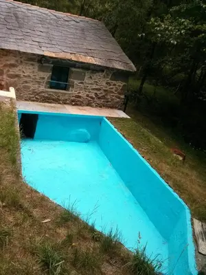 a blue swimming pool next to a stone house at Molino de Louzao in Palas de Rei