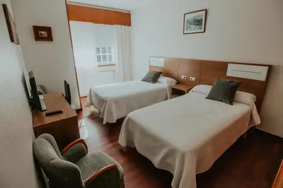 a hotel room with two beds and a chair at Hotel A Veiga in Samos