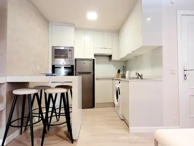 a kitchen with white cabinets and bar stools at Acogedor apartamento a la entrada de camino portugués in Santiago de Compostela