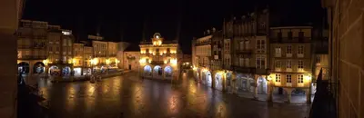 a lit up city street at night with buildings at Plaza Mayor in Ourense