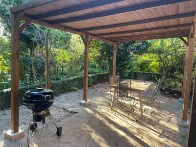 a grill under a wooden pergola with a table and a tablektop at Casa Do Bosque in Cabañas