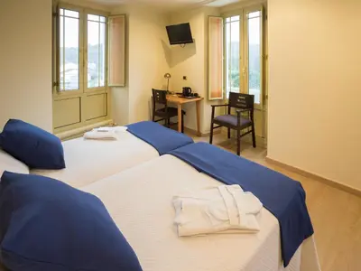 two beds in a room with a desk and a chair at Hotel Roma in Sarria