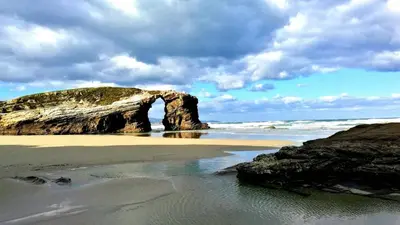 a beach with a rock arch in the ocean at Apartamento Playa San Pedro in Barreiros