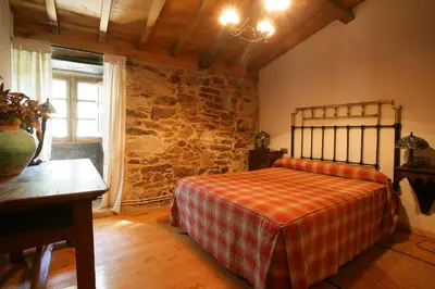 a bedroom with a bed and a stone wall at A Parada Das Bestas in Pidre
