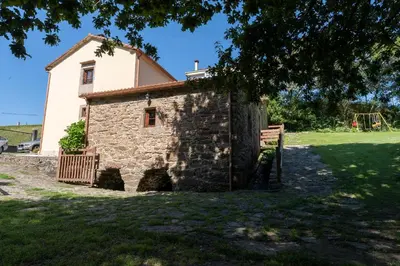 an old stone house with a playground in the background at Casa rural completa Río Sarela in Santiago de Compostela