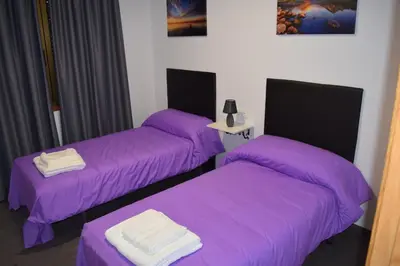 three beds in a room with purple sheets at Pensión Tasaga in O Pino