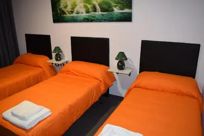 three beds in a room with orange sheets at Pensión Tasaga in O Pino