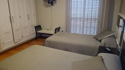 a room with two beds and a chair and a window at Hotel El Millón in Viveiro