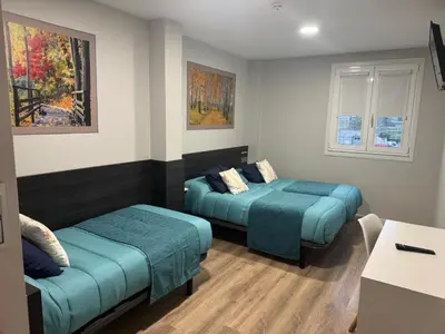 a room with two beds and a table and windows at Pension San Anton in Melide