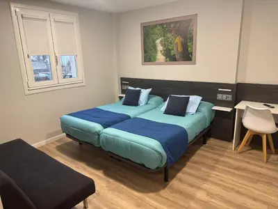 a bedroom with two beds with blue sheets and a chair at Pension San Anton in Melide