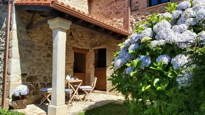a stone house with a table and blue flowers at A Casa dos Avós - Vilariño - A Coruña in Vilariño