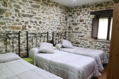a room with three beds and a stone wall at Casa Rural Madreselva in Navelgas