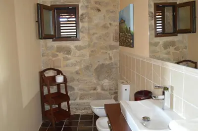 a bathroom with two sinks and a toilet and a stone wall at Airiños de Mondariz in Mondariz