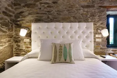 a bedroom with a white bed with a stone wall at Lar da Mota Boutique Hotel in Arzúa