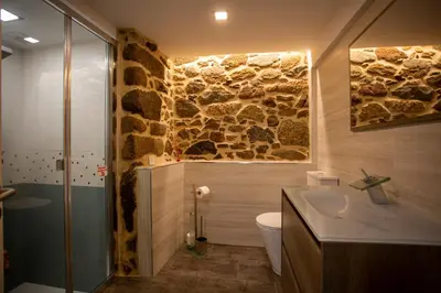 a bathroom with a stone wall and a toilet and a sink at Apartamentos Casa dos Arcos in Sober
