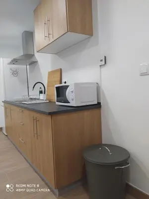 a kitchen with a microwave and a trash can at Huellas Albergue-Turístico in Portomarin