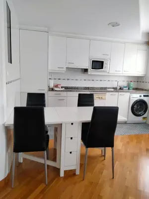 a white kitchen with white cabinets and black chairs at Piso con piscina en Sada in Sada