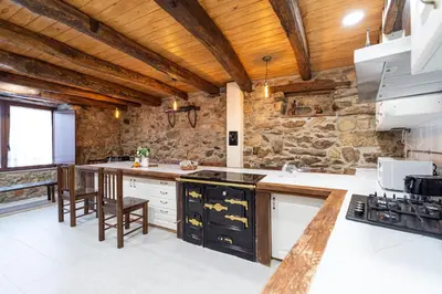 a kitchen with wooden ceilings and a stone wall at Casa Pion in Sober