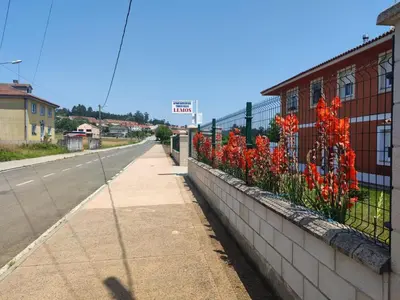 a street with red flowers on the side of a fence at Apartamentos turísticos Lemos in Pedrouzo