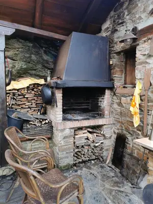a stone fireplace with two chairs in front of it at Habitación Cuadruple con derecho a Barbacoa y patio in Navia de Suarna