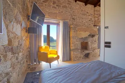 a bedroom with a yellow chair and a stone wall at Hotel As Torres da Hermida in Monterroso