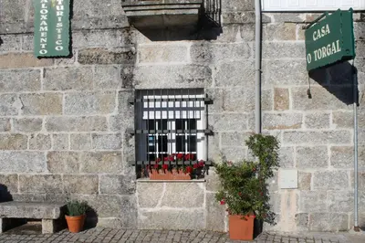 a window on a brick building with red flowers in a window grate at Casa O Torgal in Parada del Sil