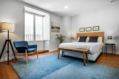 a bedroom with a bed and a chair and a window at SNÖ Camino do Eume Apartamentos in Puentedeume