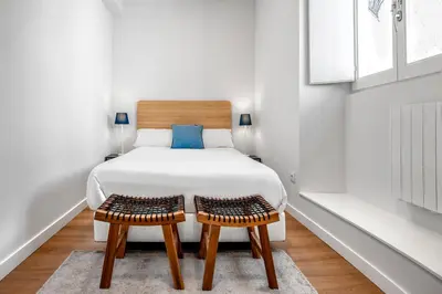 a white bedroom with a bed and two chairs at SNÖ Camino do Eume Apartamentos in Puentedeume
