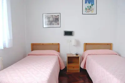 two beds in a bedroom with pink sheets and a table at Hostal Charo II in Santiago de Compostela