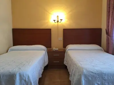 a hotel room with two beds and a light on the wall at Hotel Restaurante Derby in Carballino