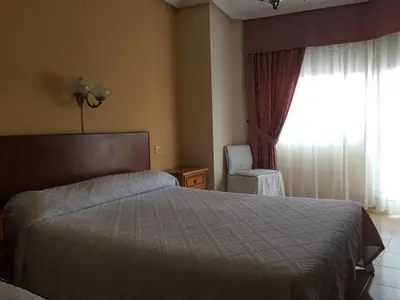 a bedroom with a bed and a window with a chair at Hotel Restaurante Derby in Carballino