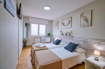 two beds in a small room with two tables at Peregrina Pensión 2 in O Pedrouzo