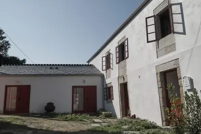 a white building with red doors and a cow standing next to it at Parga Natura Alojamiento in Parga