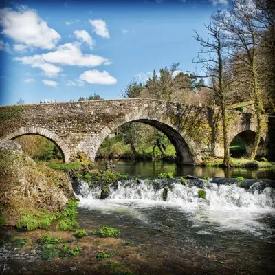 a stone bridge over a river with a waterfall at Casa Rural Camino Real in Melide