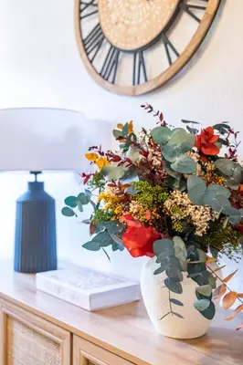a vase with flowers on a table next to a clock at Apartamentos Rurales La Laguna Somiedo in Valle de Lago