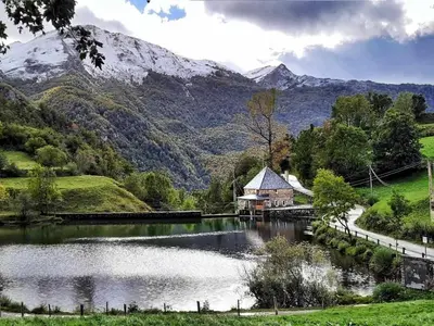 a lake with a house and mountains in the background at Apartamentos Rurales La Laguna Somiedo in Valle de Lago