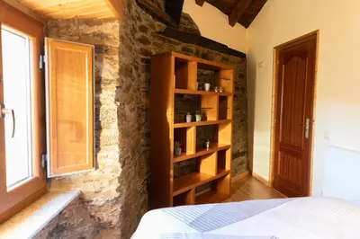 a bedroom with a stone wall with a bed and a window at As Veneiras Casa in Neipín