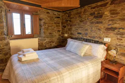 a bedroom with a bed and a stone wall at As Veneiras Casa in Neipín