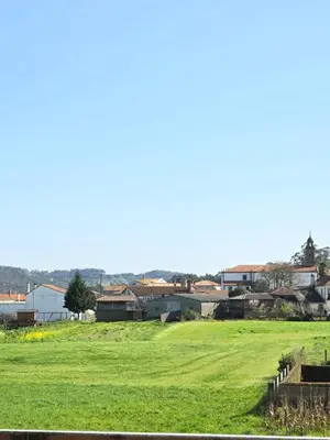 a green field with buildings in the background at Pensión Pedrouzo in O Pedrouzo