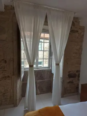 a bedroom with white curtains and a window at A Taberna de Gundián in Vedra