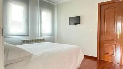 a white bedroom with a bed and a tv on the wall at Apartamentos Pantón Ribeira Sacra in Ferreira de Panton