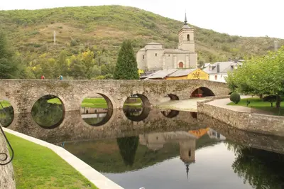 a stone bridge over a river with a church at Casa Rural La Torre De Babel in Molinaseca