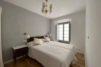 a white bedroom with a bed and a chandelier at El Taller de Doña Remedios in Mondoñedo