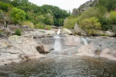 a waterfall on a rocky river with people standing near it at Altamira in Caldas de Reis