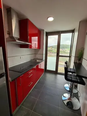 a kitchen with red cabinets and a view of the water at APARTAMENTOS VIVE in Viveiro