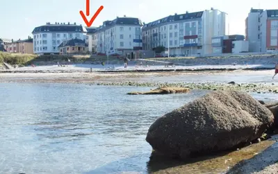 a rock in the water next to a beach with buildings at San Ciprian Marinero by I Love Norte in San Ciprián