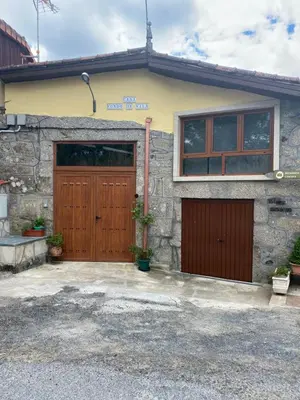 a stone house with two wooden garage doors at Casa Fondo de Vila in Chantada
