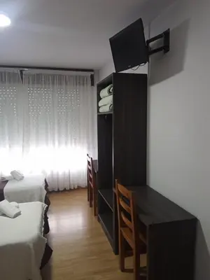 a bedroom with two beds and a desk and a window at Pensión KM66 Palas de Rei in Palas de Rei
