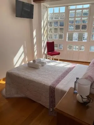 a bedroom with a bed with a red chair and a window at entrepraciñas 1 in Santiago de Compostela